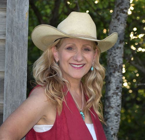 Theresa in cowgirl hat leaning against wood barn wall