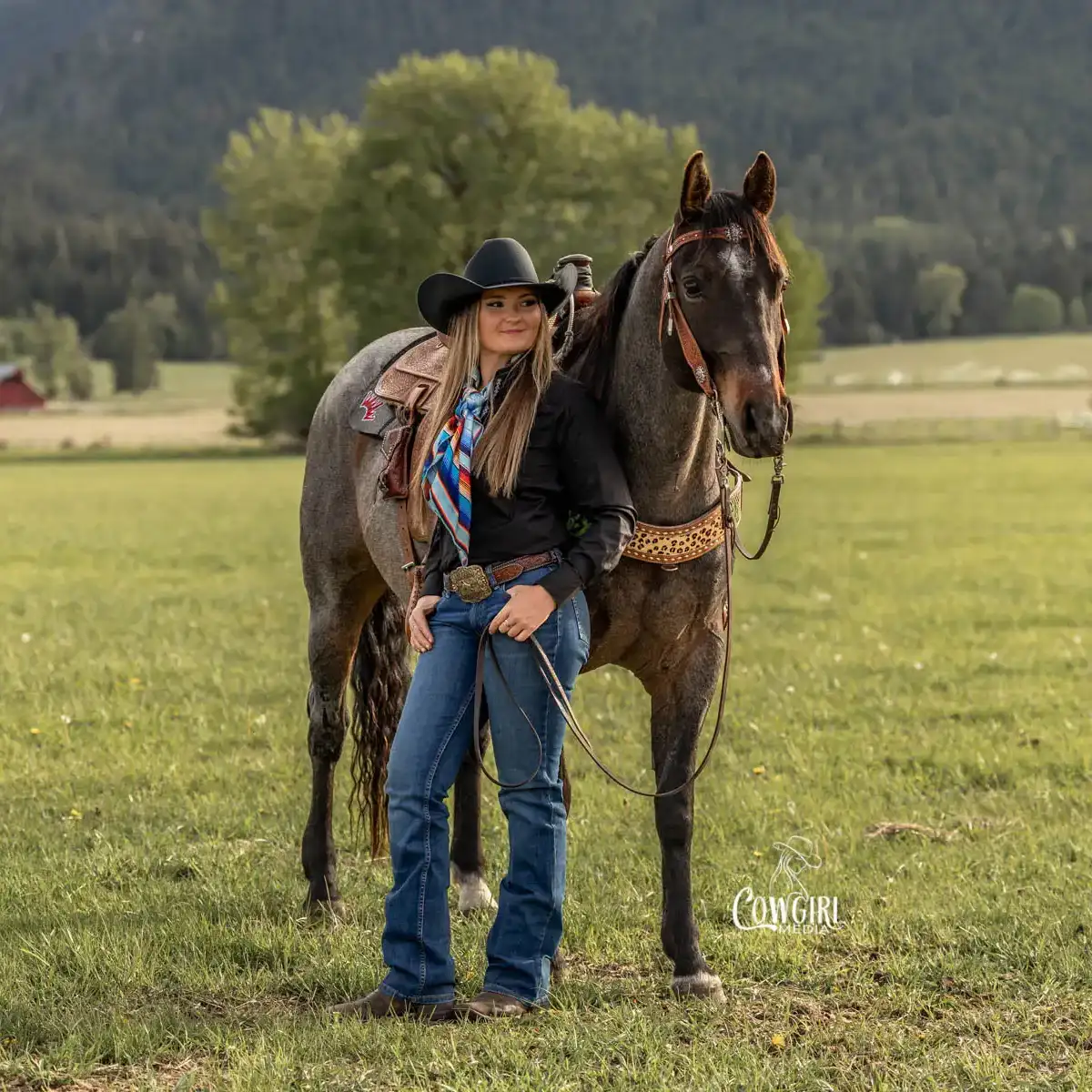 Woman standing near her bay roan horse in green field