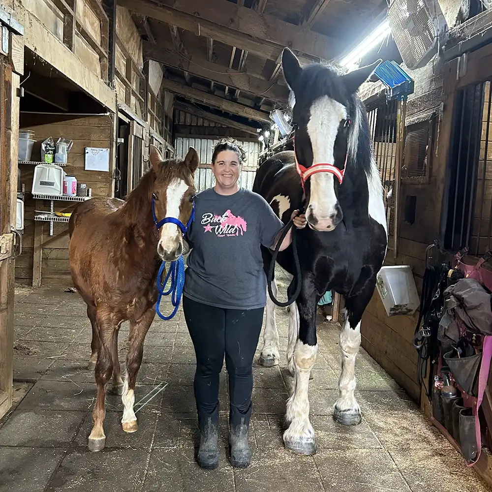 Lynn Craig standing with 2 horses in a barn