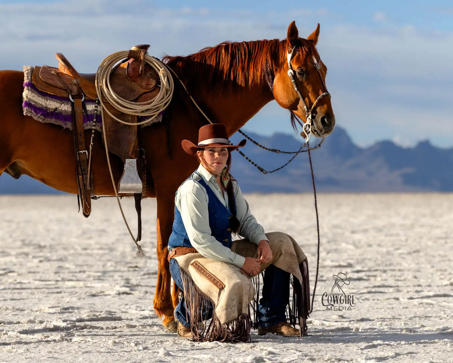 Cowgirl crouched down beside her bridle horse in the Salt Flats